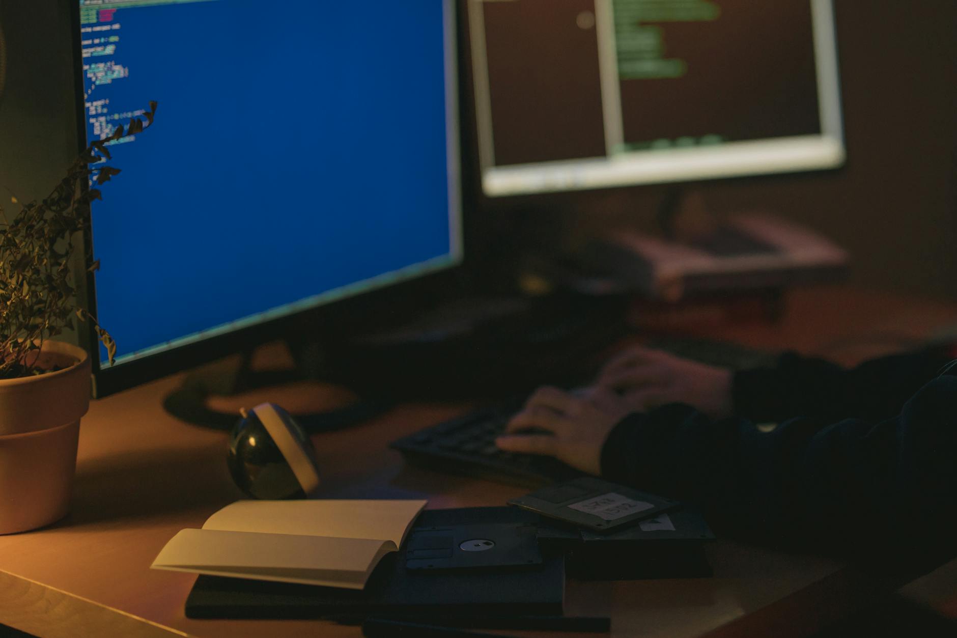 Programista pracuje przy dwóch monitorach w ciemnym pokoju