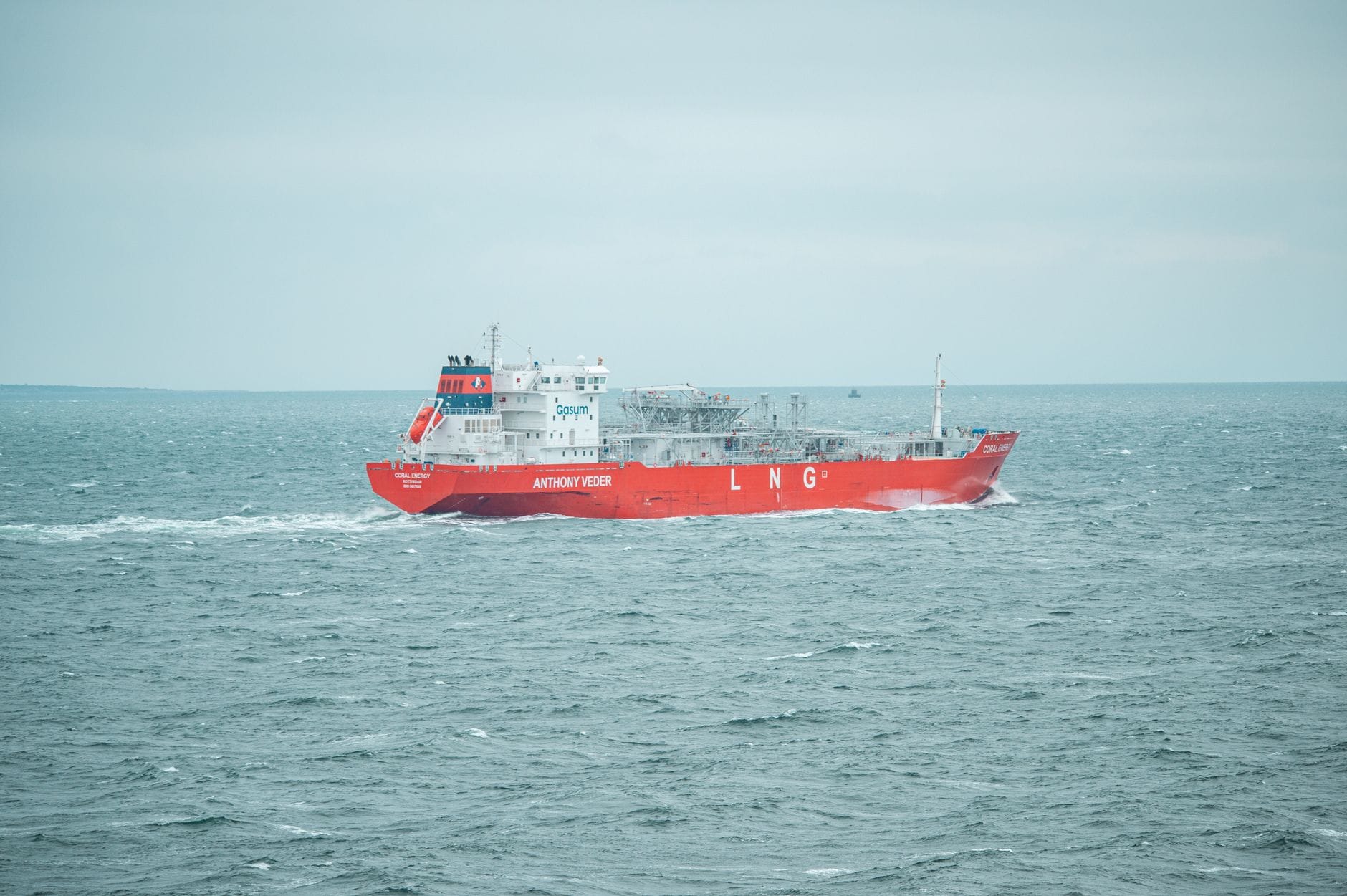 Czerwony metanowiec LNG płynie po spokojnym morzu pod zachmurzonym niebem